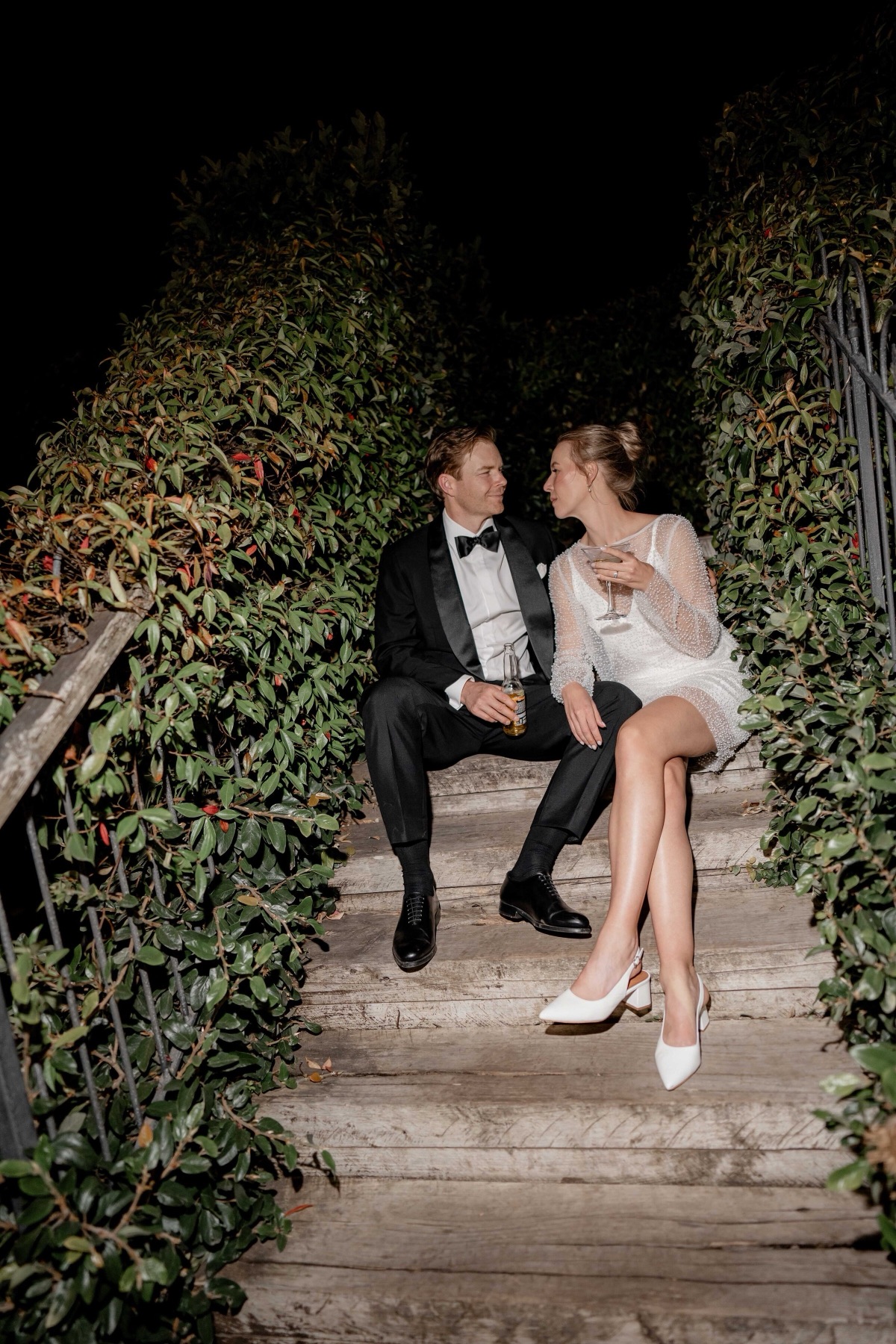 Couple sharing a drink on garden stairs at night